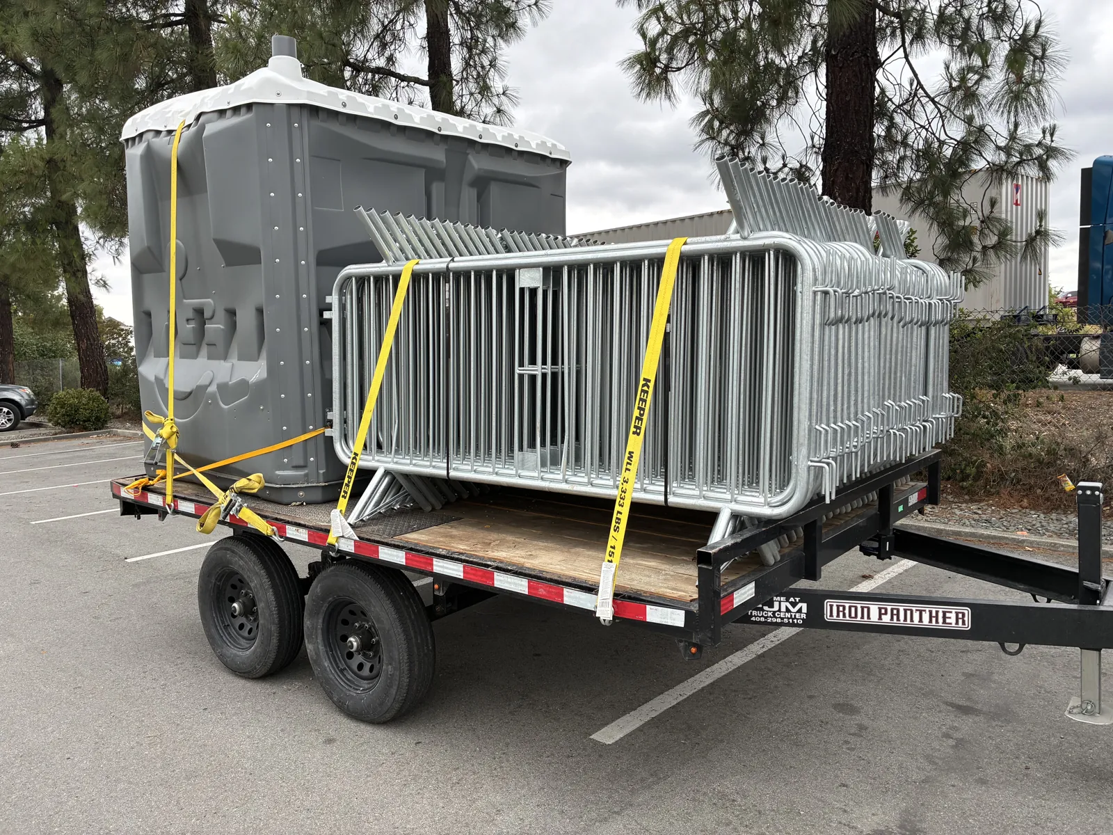 A Pro Portable Restrooms unit and temporary fence panels loaded on a single trailer