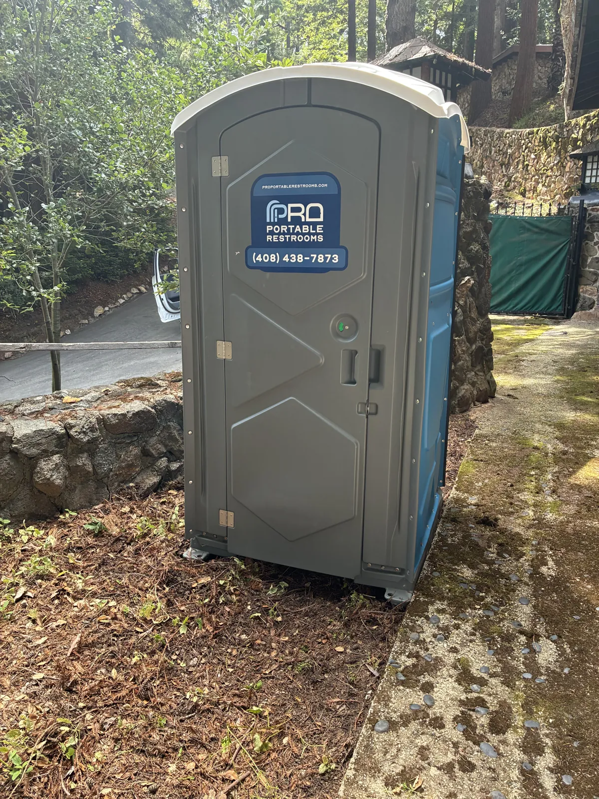 A gray Pro Portable Restrooms unit set up in a backyard garden