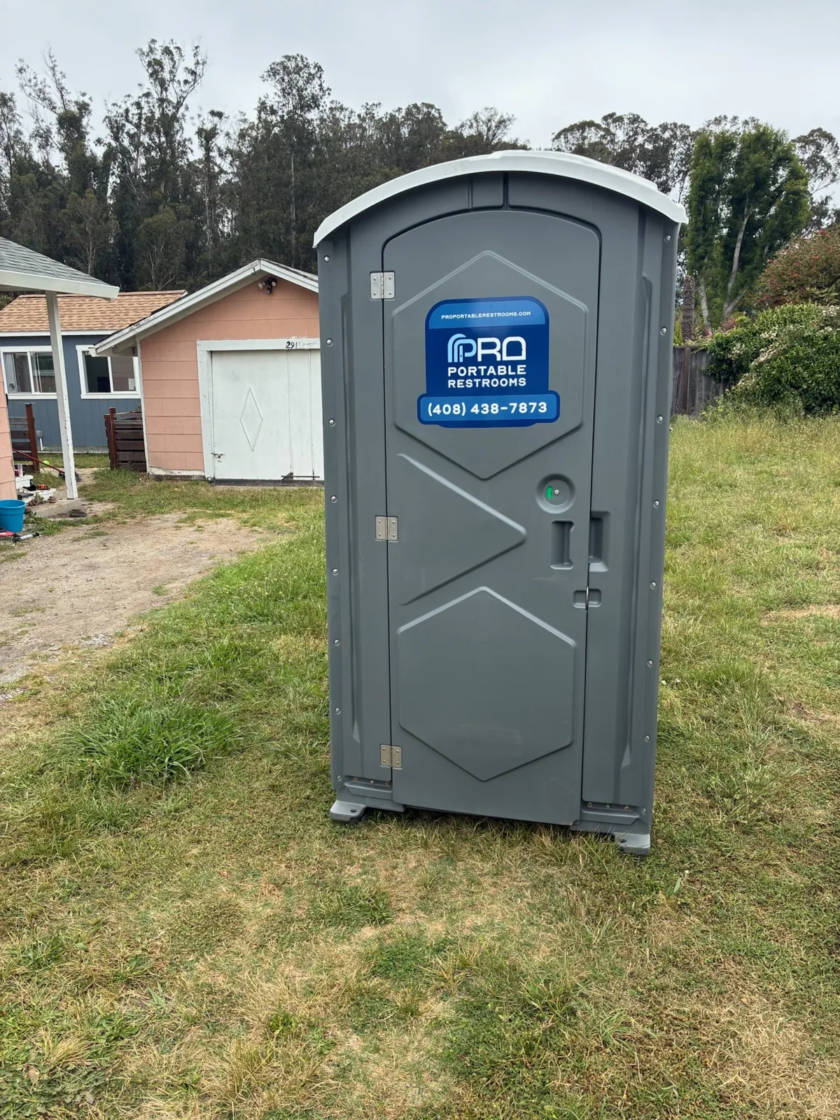 A gray Pro Portable Restrooms unit on the grass beside a home