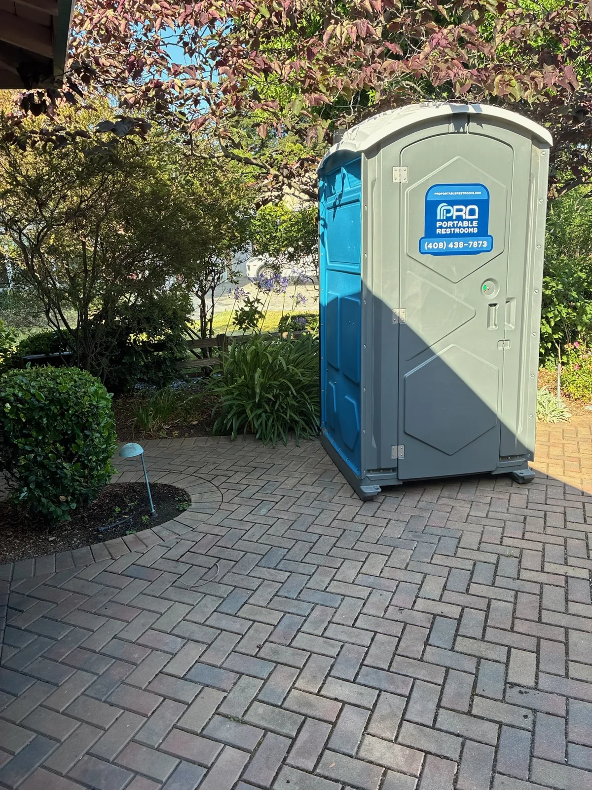 A two tone Pro Portable Restrooms unit placed on a landscaped paver patio