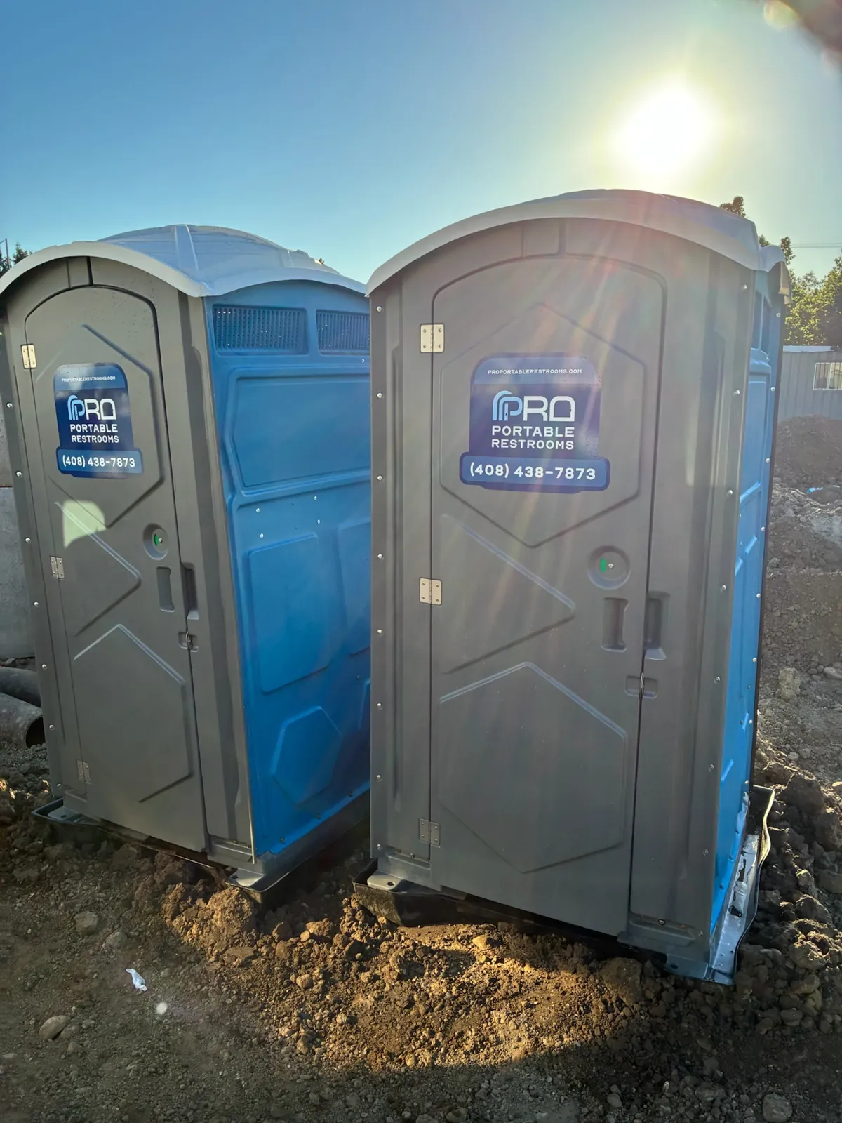 Two Pro Portable Restrooms units on a jobsite with the sun flaring behind them