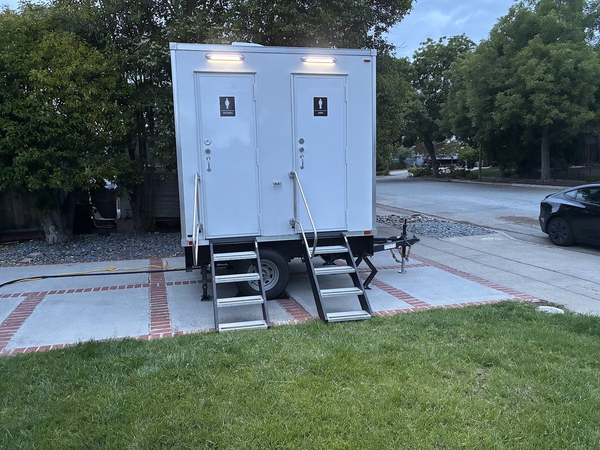 A two-station luxury restroom trailer set up on grass for an outdoor event