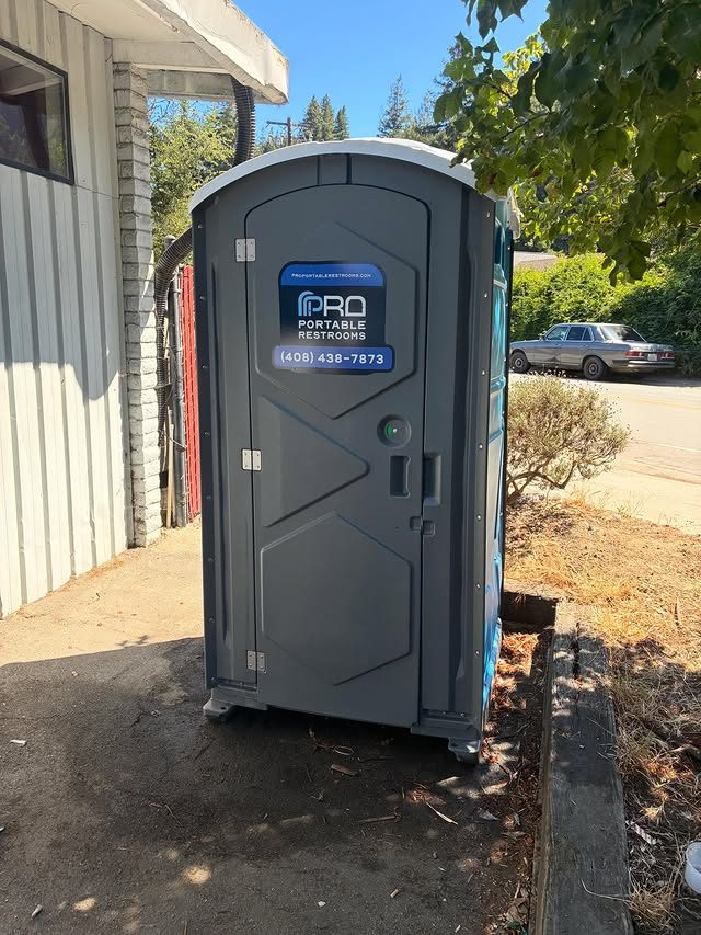 A clean porta potty positioned along a wall at a job site