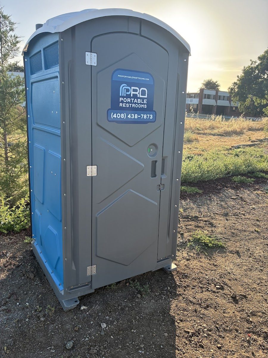 A Pro Portable Restrooms portable restroom set up in an open field at golden hour